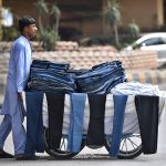 A young vendor pushes his handcart loaded with second-hand jeans and trousers along a busy road as he strives to earn a livelihood in the twin cities