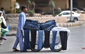 A young vendor pushes his handcart loaded with second-hand jeans and trousers along a busy road as he strives to earn a livelihood in the twin cities