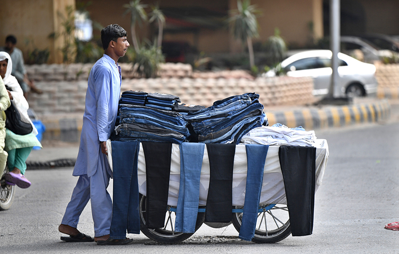 A young vendor pushes his handcart loaded with second-hand jeans and trousers along a busy road as he strives to earn a livelihood in the twin cities