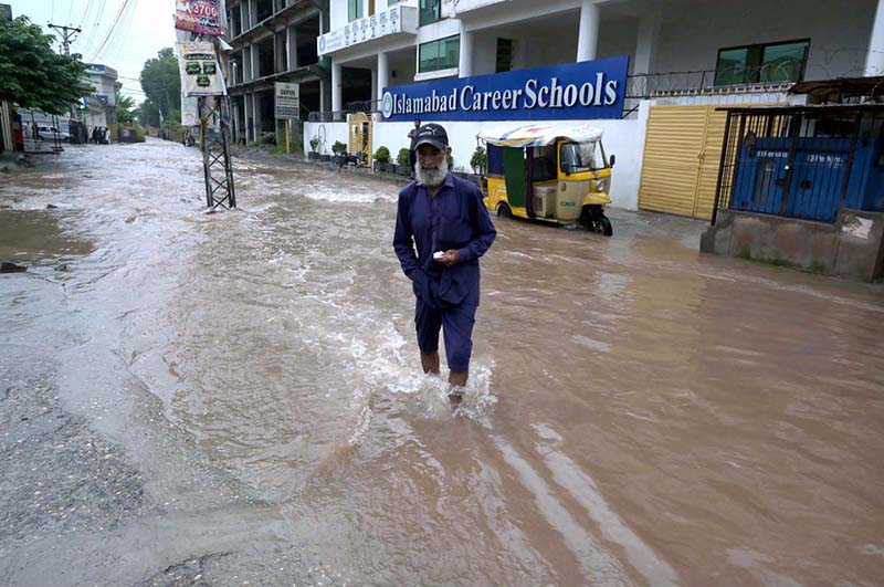 A person passing through rain water accumulated on road after heavy rain that experienced the Federal Capital