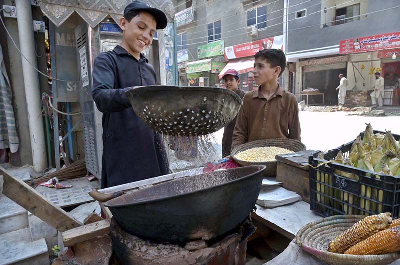 A young vendor busy roasting corn for customers at his roadside setup in Ghouri Town