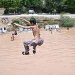 Children are jumping and bathing in a pond formed by accumulated rainwater along IGP Road