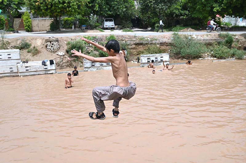 Children are jumping and bathing in a pond formed by accumulated rainwater along IGP Road