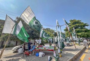 A seasonal woman vendor waits for customers while displaying Pakistani national flags and Independence Day celebration items along Murree Road in Rawalpindi ahead of August 14.