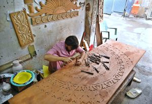 A craftsman hand-carves intricate designs on a wooden door using traditional tools at his workshop in twin cities.
