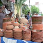 An elderly vendor busy arranging and displaying clay made pots on his handcart to attract the customers