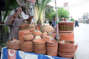 An elderly vendor busy arranging and displaying clay made pots on his handcart to attract the customers