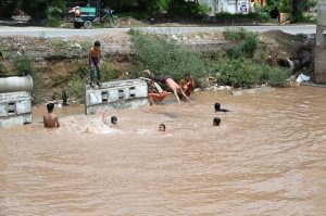 Children are jumping and bathing in a pond formed by accumulated rainwater along IGP Road