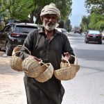 An elderly vendor displaying baskets to attract the customers while shuttling on the road in the Federal Capital