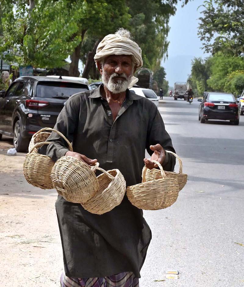 An elderly vendor displaying baskets to attract the customers while shuttling on the road in the Federal Capital
