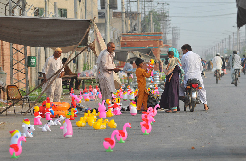 A family purchases colorful toys for a child from a roadside vendor at a temporary stall in the city