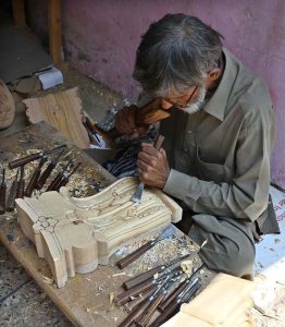 An elderly carpenter carves intricate designs into a wooden piece at handcrafted woodwork in the federal capital.