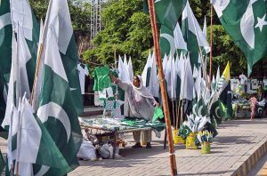 In connection with Independence Day celebrations, a female vendor displays children's clothing featuring Pakistani national colors and designs at her roadside stall on Murree Road.