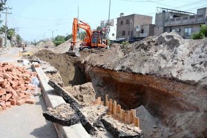 Workers fill the dug-up area with heavy machinery after laying the sewerage pipeline during ongoing development work in Mumtazabad