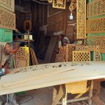 An artisan skillfully shapes a wooden panel with a jigsaw while crafting intricate traditional jali work at a local workshop
