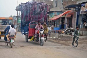 A heavily loaded rickshaw carrying iron beds travels on Shaheenabad Road, violating traffic safety regulations.
