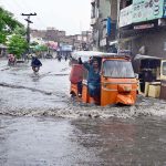 Auto rickshaws passing through rain water accumulated on road after heavy rain in the city