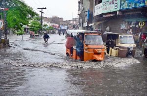 Auto rickshaws passing through rain water accumulated on road after heavy rain in the city