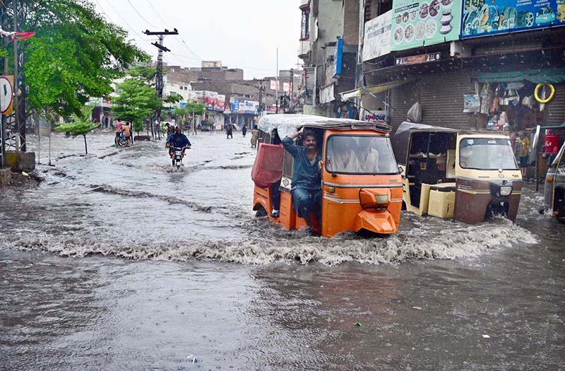 Auto rickshaws passing through rain water accumulated on road after heavy rain in the city