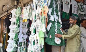 A shopkeeper displays national flag-themed kids outfits and festive apparel at Anarkali Bazaar as markets gear up for Pakistan's Independence Day celebrations.