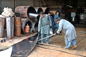 A worker cuts a steel sheet with large metal shears at a workshop on Gawal Mandi Road in twin cities.