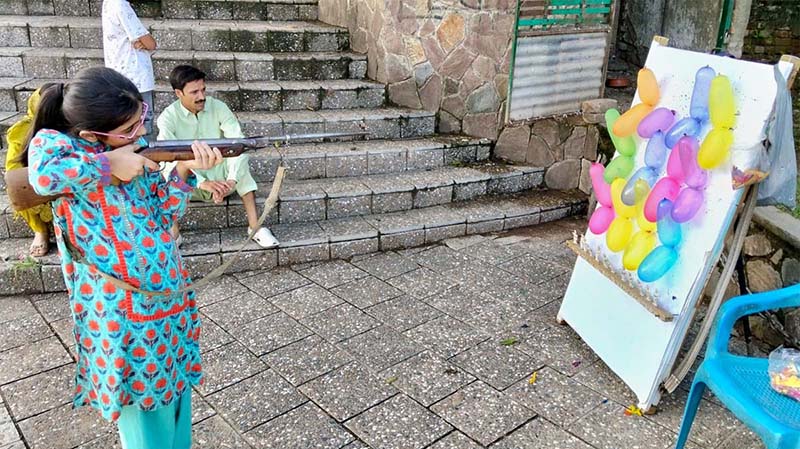 A young girl takes careful aim at a colourful array of balloons during a shooting game at Shakarpatrian area in the Federal Capital