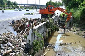 CDA workers are using heavy machinery to clear a drainage channel that had become clogged with debris following heavy monsoon rains, causing water to overflow onto the road and disrupt the flow of traffic.