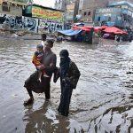 A family makes its way through rainwater accumulated on a road during heavy rainfall in the city