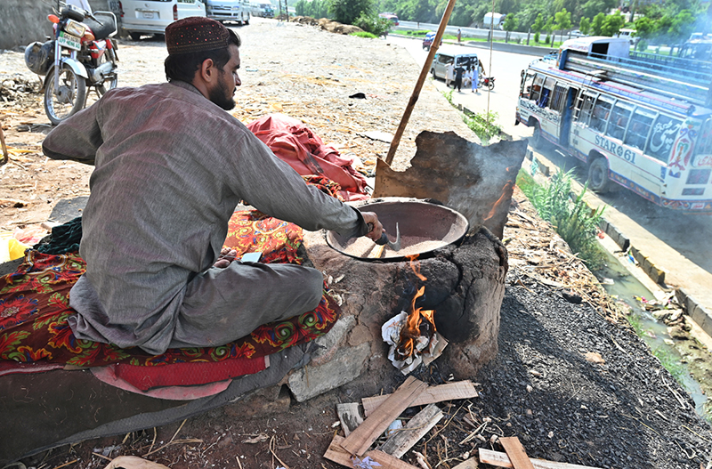 A vendor roasts corn cobs at his roadside setup near the Pirwadhai area in the Federal Capital