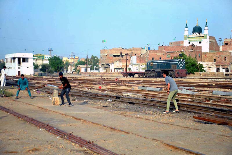 A group of youngsters playing cricket along railway tracks near railway station