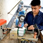 A young worker operates a key-cutting machine at a workshop