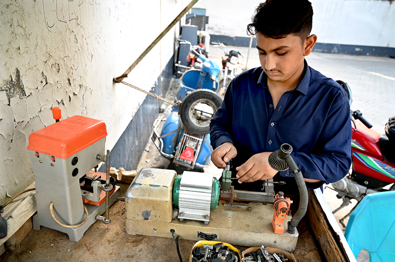 A young worker operates a key-cutting machine at a workshop
