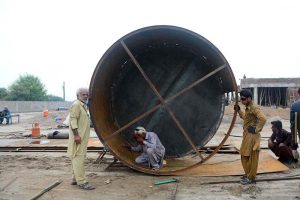 A worker welds a large steel oil storage tank while colleagues assist during fabrication at a workshop on Muzaffargarh Road.