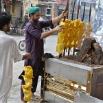 A vendor arranges skewered chicken over hot coals at a roadside food stall