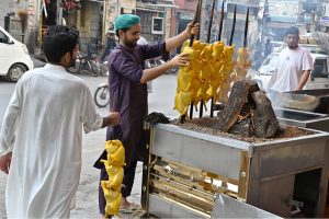 A vendor arranges skewered chicken over hot coals at a roadside food stall