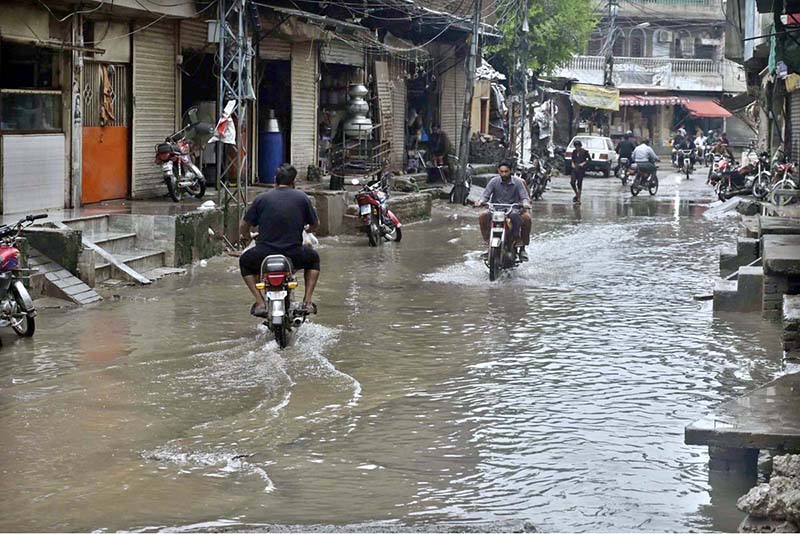 Motorcyclists navigate a flooded road following a torrential monsoon rain spell at Imam bara chowk in the twin cities