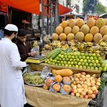 A vendor arranges and displays seasonal fruits to attract customers on his cart along a roadside