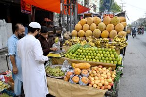 A vendor arranges and displays seasonal fruits to attract customers on his cart along a roadside