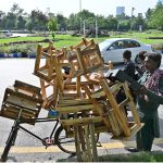 A vendor loads a bicycle with wooden stools and furniture items to sell in different areas of the Federal Capital