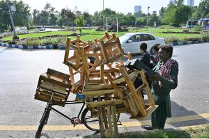 A vendor loads a bicycle with wooden stools and furniture items to sell in different areas of the Federal Capital