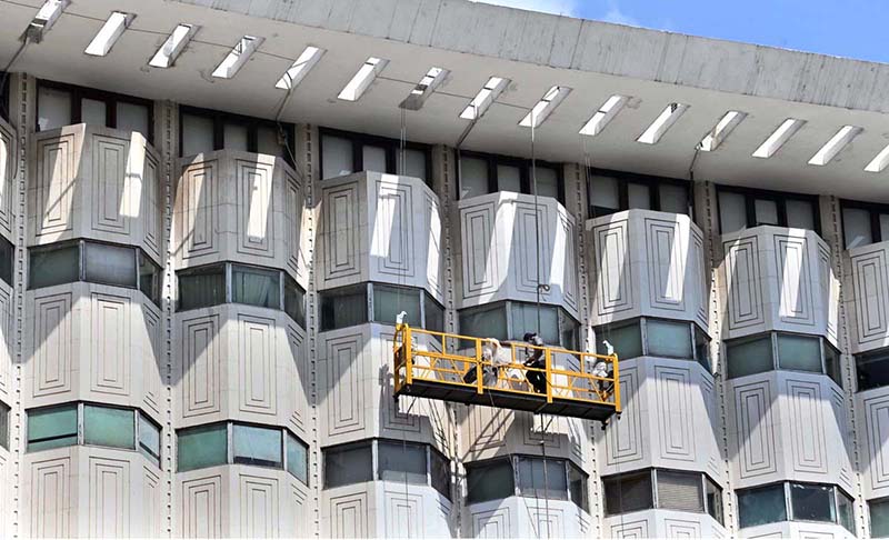Workers suspended on a hanging scaffold carry out cleaning and maintenance of the iconic WAPDA House building