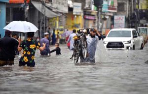Motorcyclists navigate a flooded road following a torrential monsoon rain spell at Imam bara chowk in the twin cities