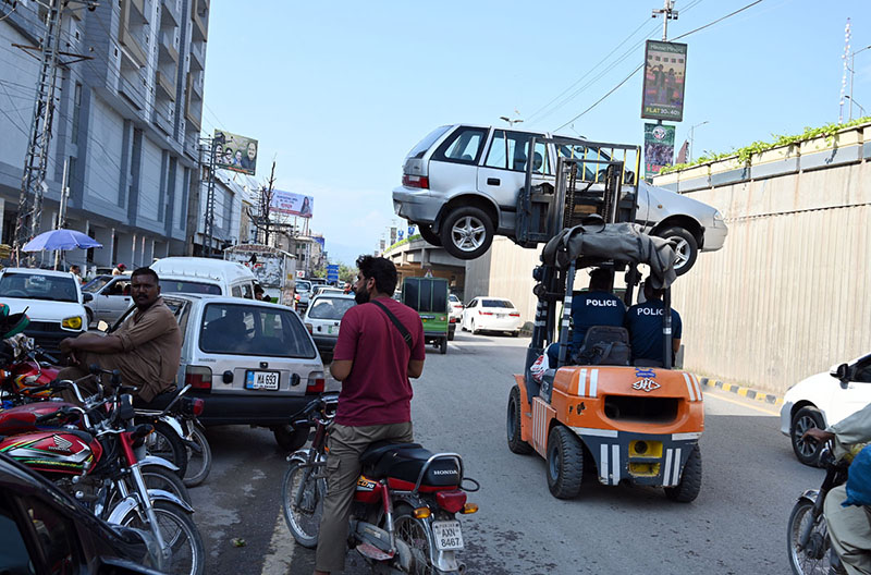 Traffic police use a forklift to remove an illegally parked vehicle from the roadside as part of an anti-encroachment operation