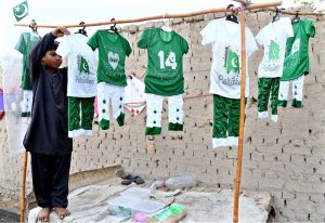A child vendor displays Independence Day-themed children's dresses to attract customers at Wada Mahar village.