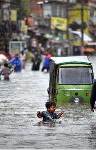 A child stands amid floodwater as an auto-rickshaw makes its way through the inundated street following heavy monsoon rains in Dhoke Khabba