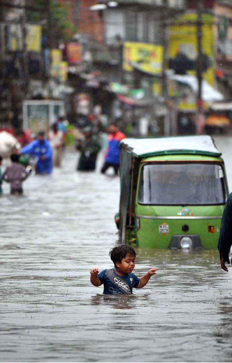 A child stands amid floodwater as an auto-rickshaw makes its way through the inundated street following heavy monsoon rains in Dhoke Khabba