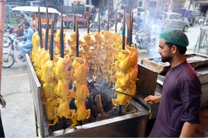 A vendor roasts chickens on skewers over an open flame at his roadside stall along Saidpur Road in the city