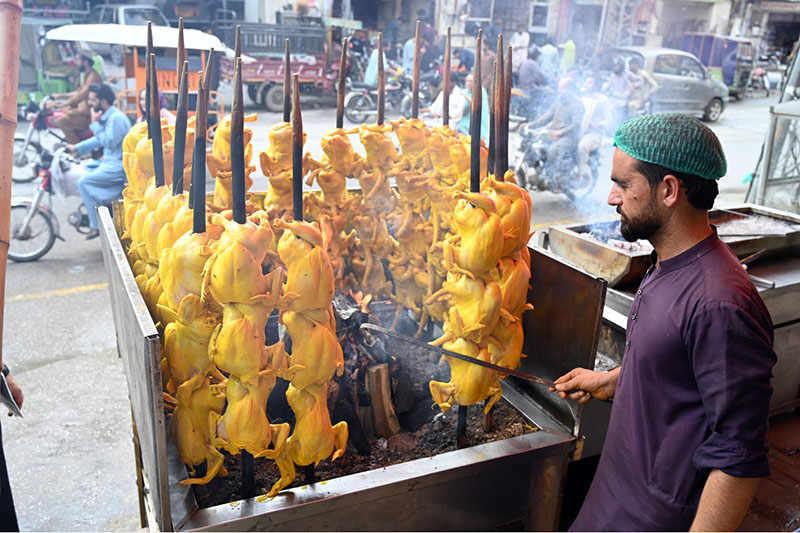 A vendor roasts chickens on skewers over an open flame at his roadside stall along Saidpur Road in the city