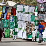 Two women pass by Independence Day-themed, national-colour dresses for children displayed by a street vendor at Old Bus Stand Road ahead of Independence Day celebrations