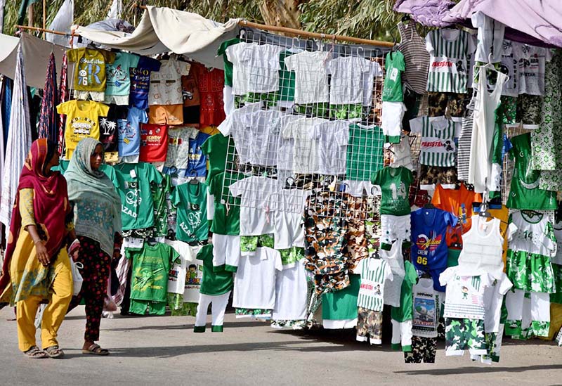 Two women pass by Independence Day-themed, national-colour dresses for children displayed by a street vendor at Old Bus Stand Road ahead of Independence Day celebrations